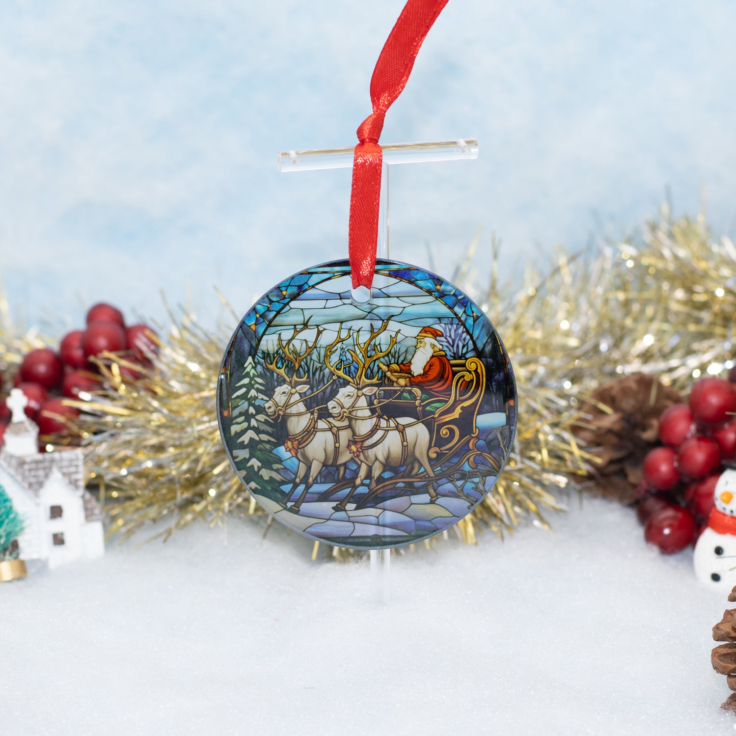 A round Christmas ornament featuring a stained-glass style illustration of Santa Claus in his sleigh with reindeer, hanging from a red ribbon against a snowy, festive background with gold tinsel and red berries.