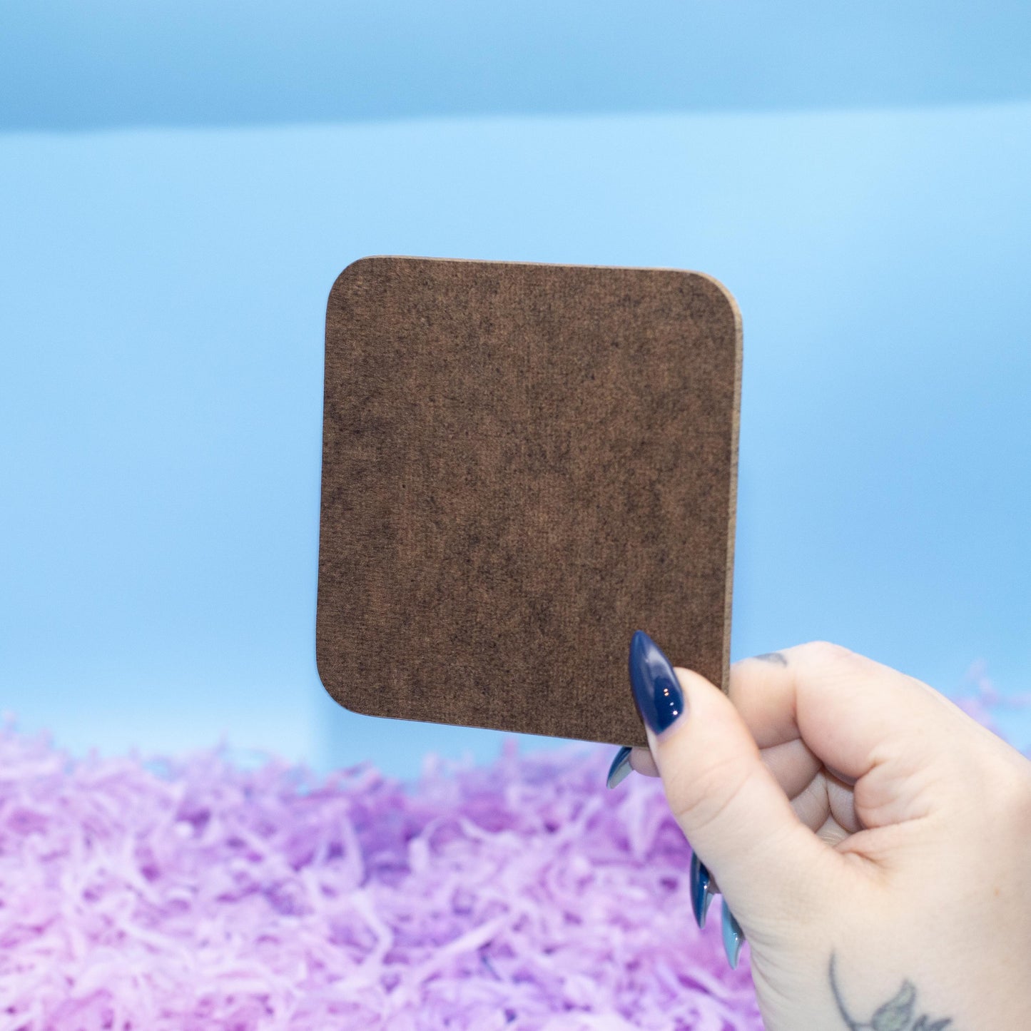 Showing Reverse of Square hard backed coaster featuring a colourful pattern of glossy pastel heart candies, set against a blue background with purple shredded paper.
