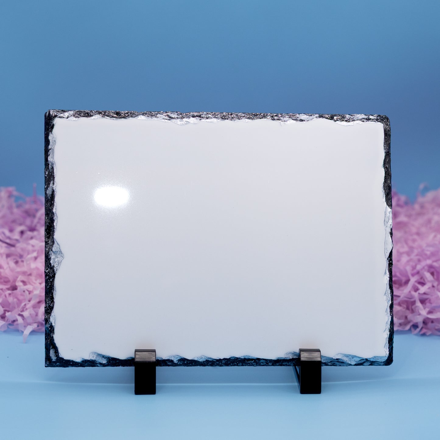 A rectangular plaque with a rough dark natural border, displayed on two small black stands against a blue background with pink decorative filler on the sides.