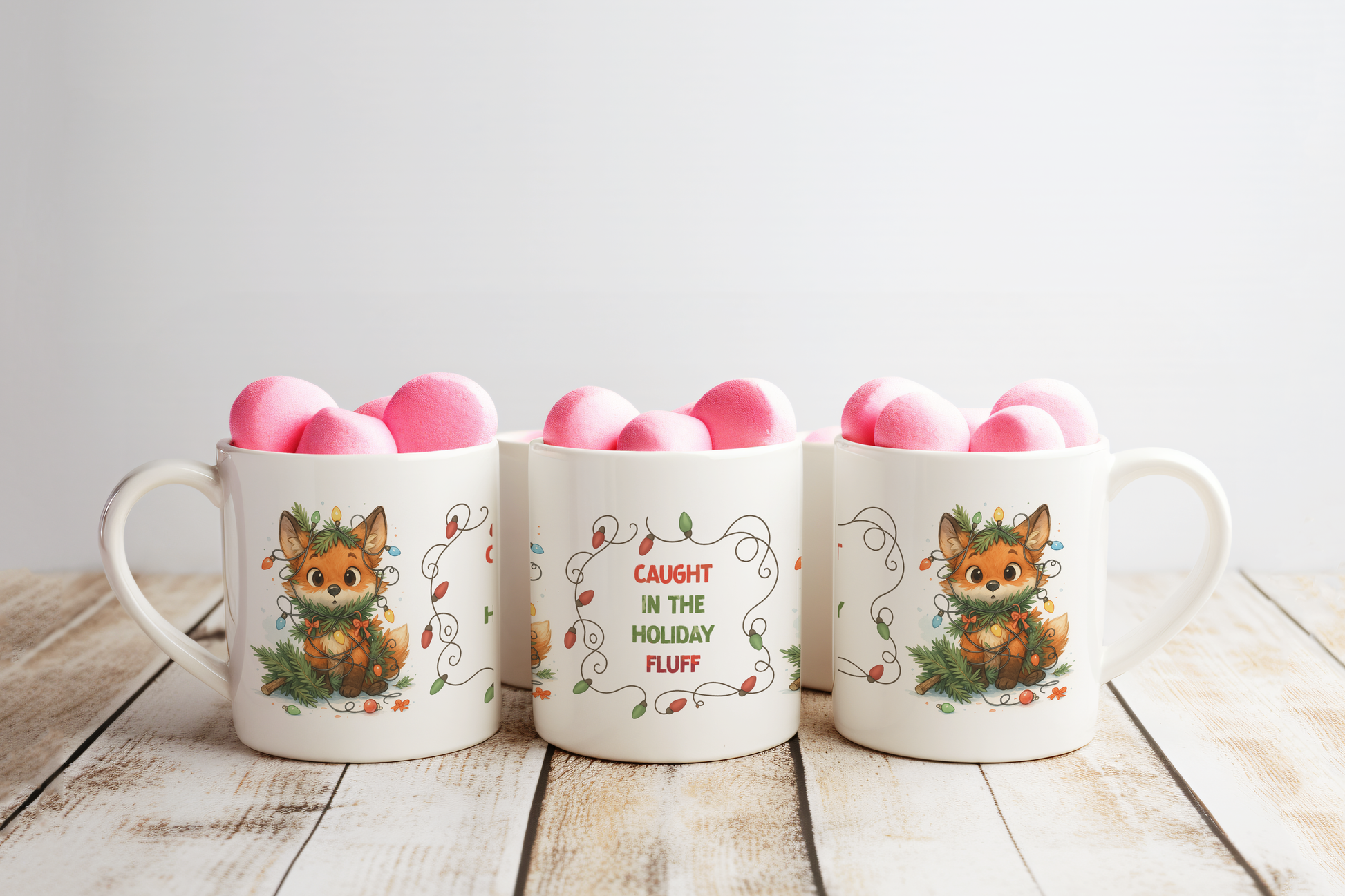 Three white ceramic mugs with holiday fox illustrations arranged on a rustic wooden surface against a light gray background.