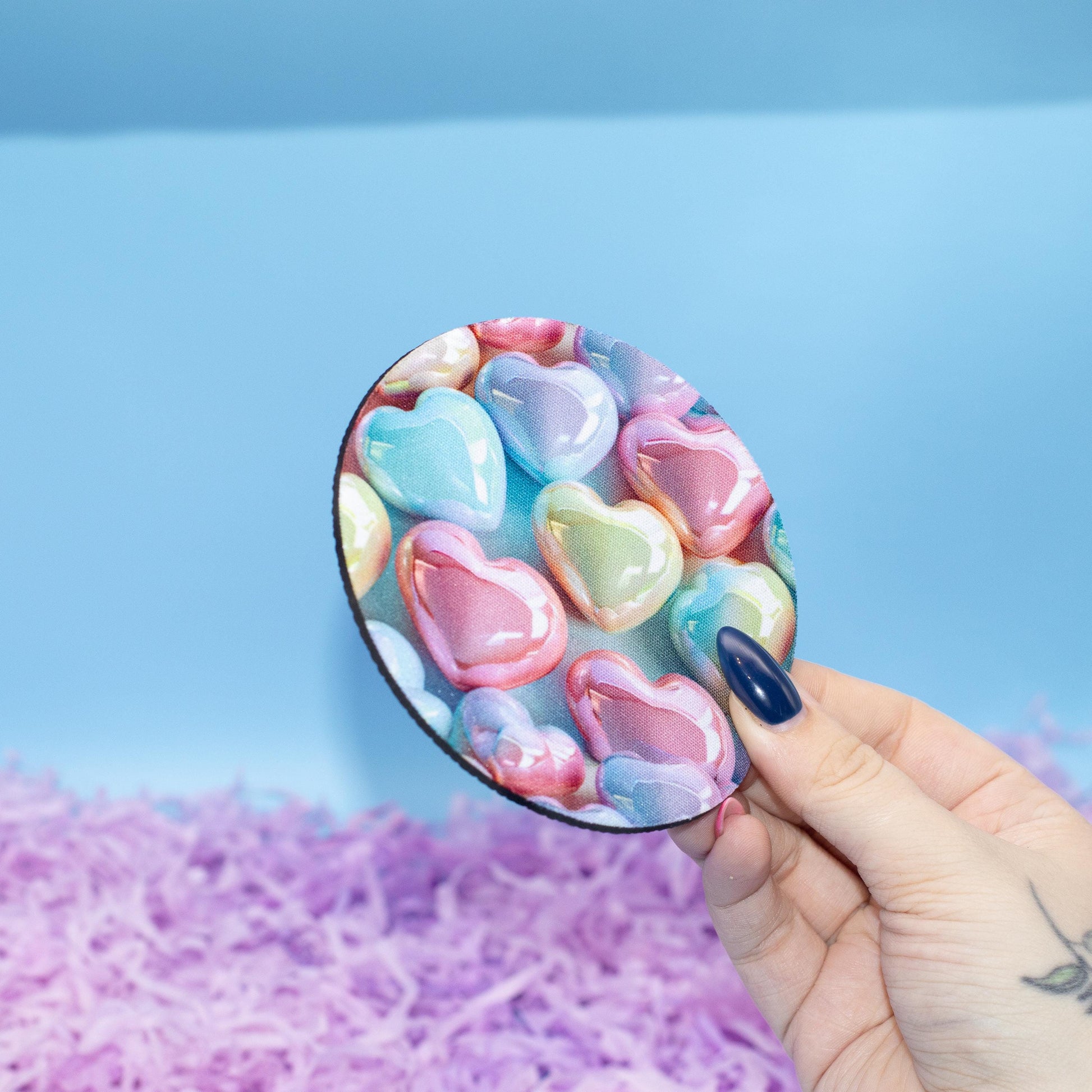Round coaster featuring a colourful pattern of glossy heart-shaped candy set against a light blue background 