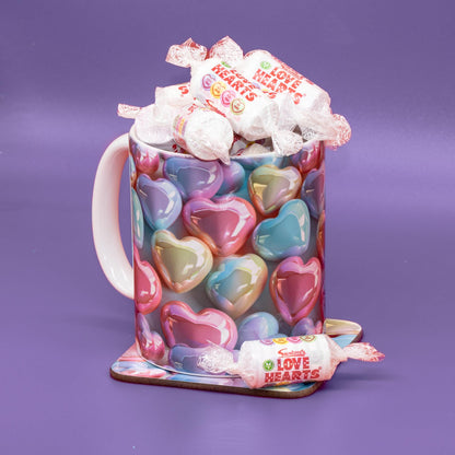 A ceramic mug covered in pastel heart candies, filled with wrapped chocolates and topped with a wrapped candy, set against a solid purple background.