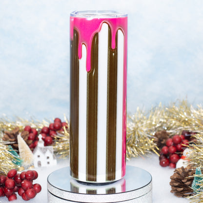 A tall, tumbler with a printed design of vertical brown and white stripes and bright pink dripping accents, displayed on a silver pedestal with holiday decorations in the background.