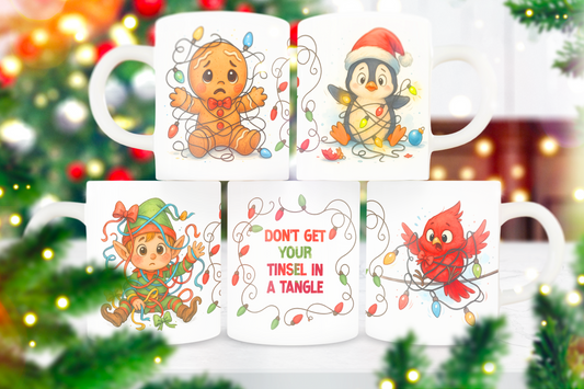 Five white ceramic mugs with Christmas-themed illustrations are arranged in two rows against a blurred festive background of Christmas trees and lights. The top row shows a gingerbread man tangled in holiday lights, a penguin in a Santa hat, and a child with an elf hat.