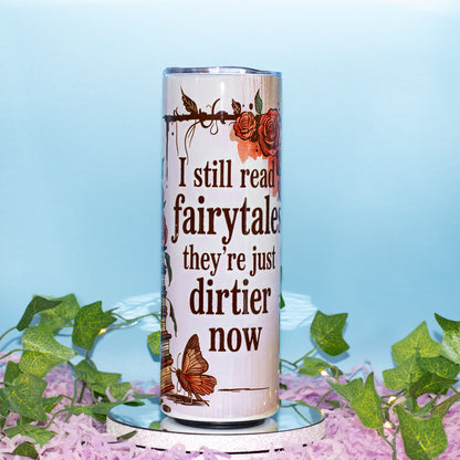 A tall insulated tumbler with a clear lid, featuring the printed phrase 'I still read fairytales they're just dirtier now' in dark brown text, decorated with orange and red roses and a butterfly on a light beige background.