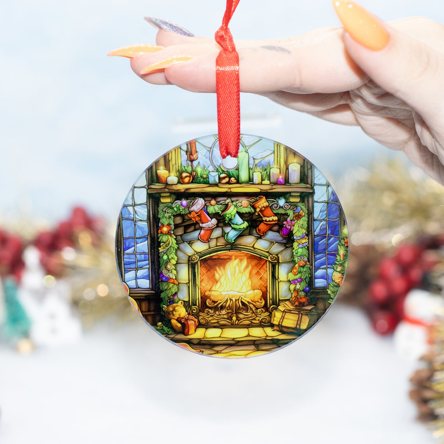A hand holds a round hanging ornament featuring a colorful stained-glass-style fireplace scene with stockings, candles, and a red ribbon loop at the top.
