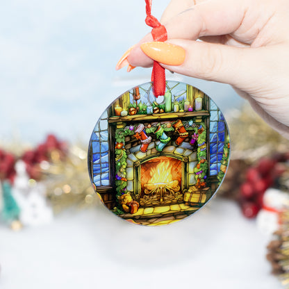 A hand holds a round Christmas ornament featuring a colourful stained-glass-style fireplace scene with stockings, candles, and a red hanging cord. The background is softly blurred with festive decorations.