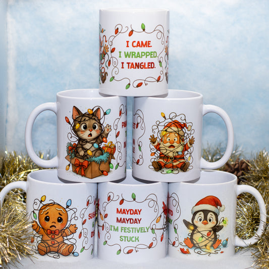 A stack of six white ceramic mugs decorated with festive Christmas illustrations and holiday-themed quotes, arranged in a pyramid on a light blue textured background with gold tinsel.