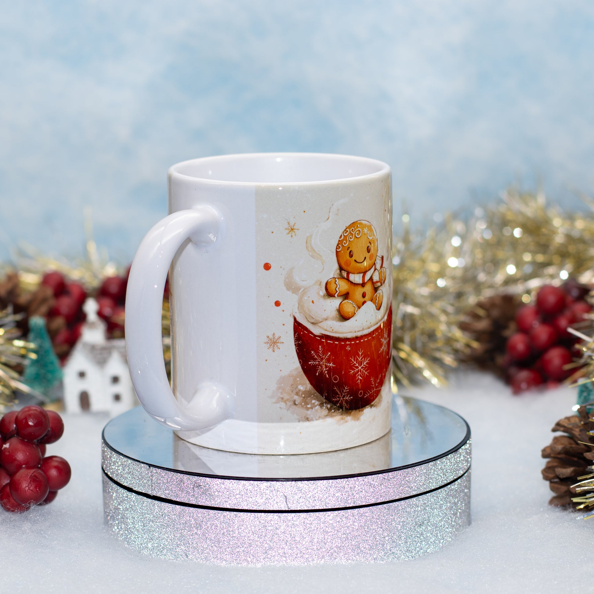 A white ceramic mug with a Christmas gingerbread man illustration sitting in a red mug of hot cocoa, displayed on a round mirrored stand with a glittery base against a festive holiday background.
