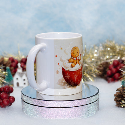 A white ceramic mug with a Christmas gingerbread man illustration sitting in a red mug of hot cocoa, displayed on a round mirrored stand with a glittery base against a festive holiday background.