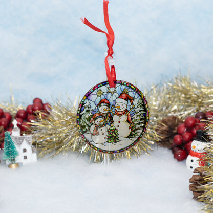 A round Christmas ornament featuring two snowmen under a starry night sky, hanging from a red ribbon. The ornament is styled on a white surface with gold tinsel, red berries, pinecones, and a small white house.
