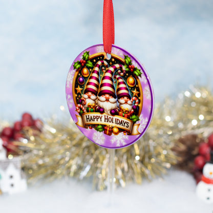 A round purple Christmas ornament featuring three gnomes with striped hats and a 'Happy Holidays' banner, hanging by a red ribbon against a festive blurred holiday background.