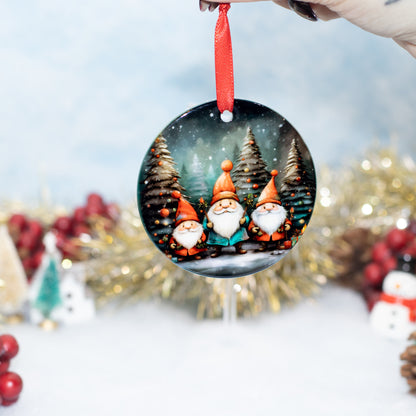 A round Christmas ornament hanging from a red ribbon, held by a hand against a festive blurred background with gold tinsel, red berries, and snowman decorations. The ornament features three gnome characters standing in a snowy forest at night.