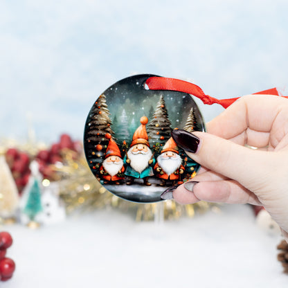 A hand holds a round Christmas ornament featuring three smiling gnomes in a snowy forest. The ornament has a red ribbon loop and is photographed against a softly blurred festive background with gold tinsel and red berries.