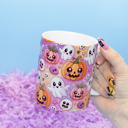 white ceramic mug decorated with a cute, colorful pattern of smiling pumpkins, ghosts, and skulls on a purple background, set against a light blue backdrop with purple shredded paper.