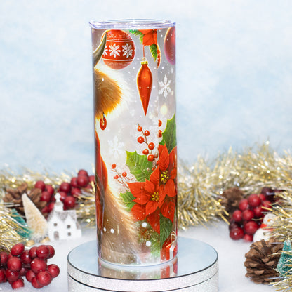 A tall cylindrical glass tumbler with a clear lid, decorated with a festive Christmas design featuring red poinsettias, ornaments, snowflakes, displayed on a silver pedestal with holiday decorations in the background.