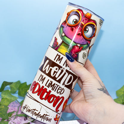 A hand holds a cylindrical plastic container featuring a colourful cartoon dino and the text 'I'M NOT weird, I'M LIMITED EDITION' 