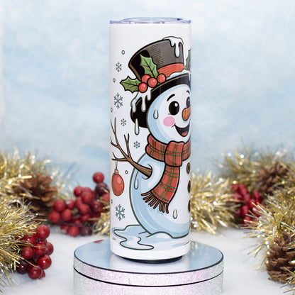 A white insulated tumbler with a cartoon snowman design, standing on a round silver pedestal. The tumbler features a festive illustration of a snowman wearing a black top hat with red berries, a red plaid scarf, and a twig arm.