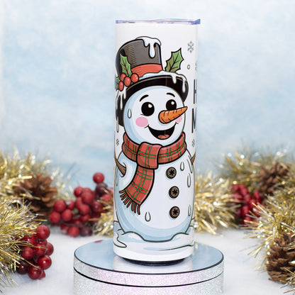 A tall white insulated tumbler with a cartoon snowman design wearing a black top hat and red plaid scarf, displayed on a round silver pedestal with holiday tinsel and red berries in the background.