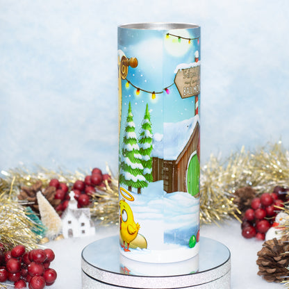 A cylindrical Christmas tumbler showing decorative light with a winter village illustration, displayed on a mirrored pedestal with holiday tinsel, red berries, and pinecones around it.