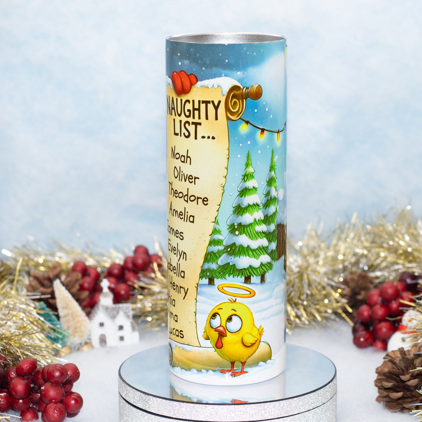 A cylindrical Christmas ornament with a festive 'Naughty List' design, featuring a cartoon baby turkey, snow-covered pine trees, and a list of names, displayed on a silver stand with holiday decorations in the background.