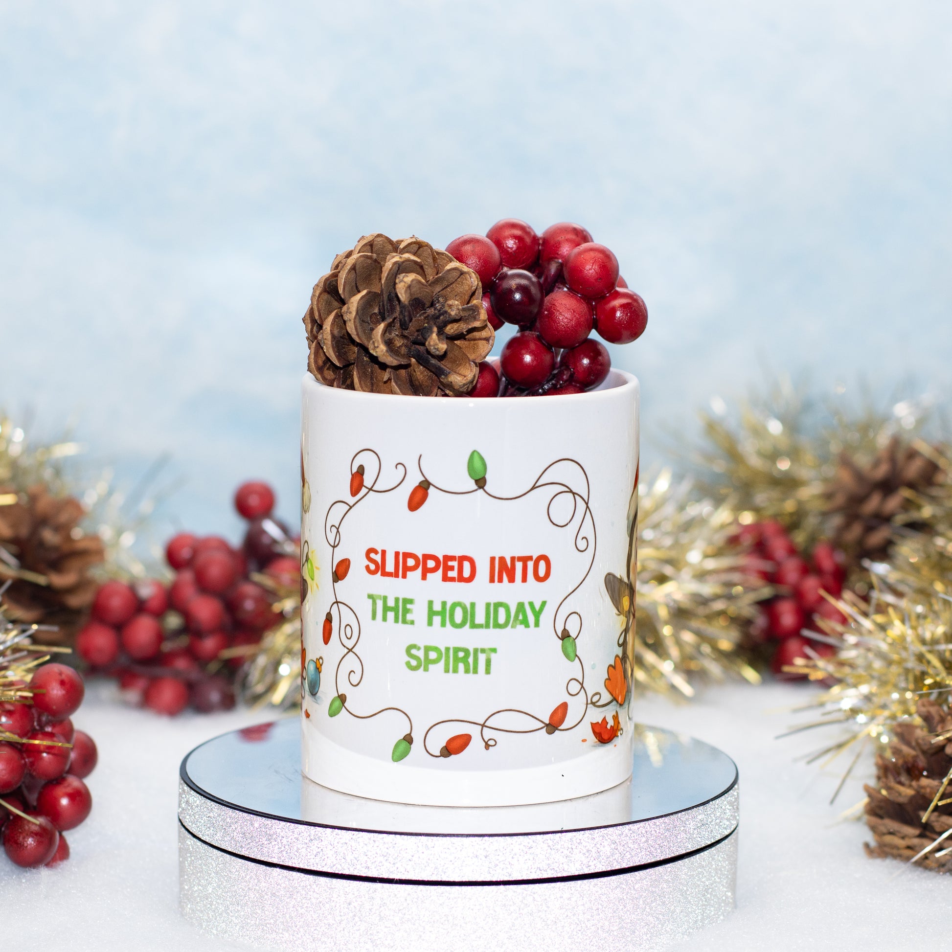 A white ceramic holiday mug with the phrase 'SLIPPED INTO THE HOLIDAY SPIRIT' in red and green lettering, surrounded by a decorative vine border.
