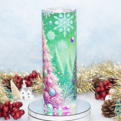 A tall cylindrical tumbler with a clear lid, featuring a festive Christmas tree design in shades of green, pink, purple, and blue. The tumbler is displayed on a silver pedestal with holiday decorations like red berries, pinecones, and gold tinsel in the background.