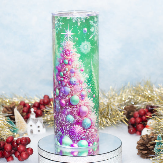 A tall Stainless Steel Tumbler featuring a colourful printed Christmas tree design with pink, purple, and green ornaments, set on a silver pedestal with holiday decorations in the background.