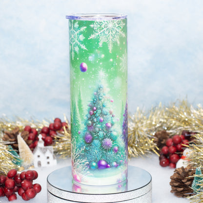 A tall cylindrical tumbler with a festive winter holiday design, featuring a green background with snowflakes, a decorated Christmas tree, and purple ornaments, displayed on a silver pedestal with holiday decorations in the background.