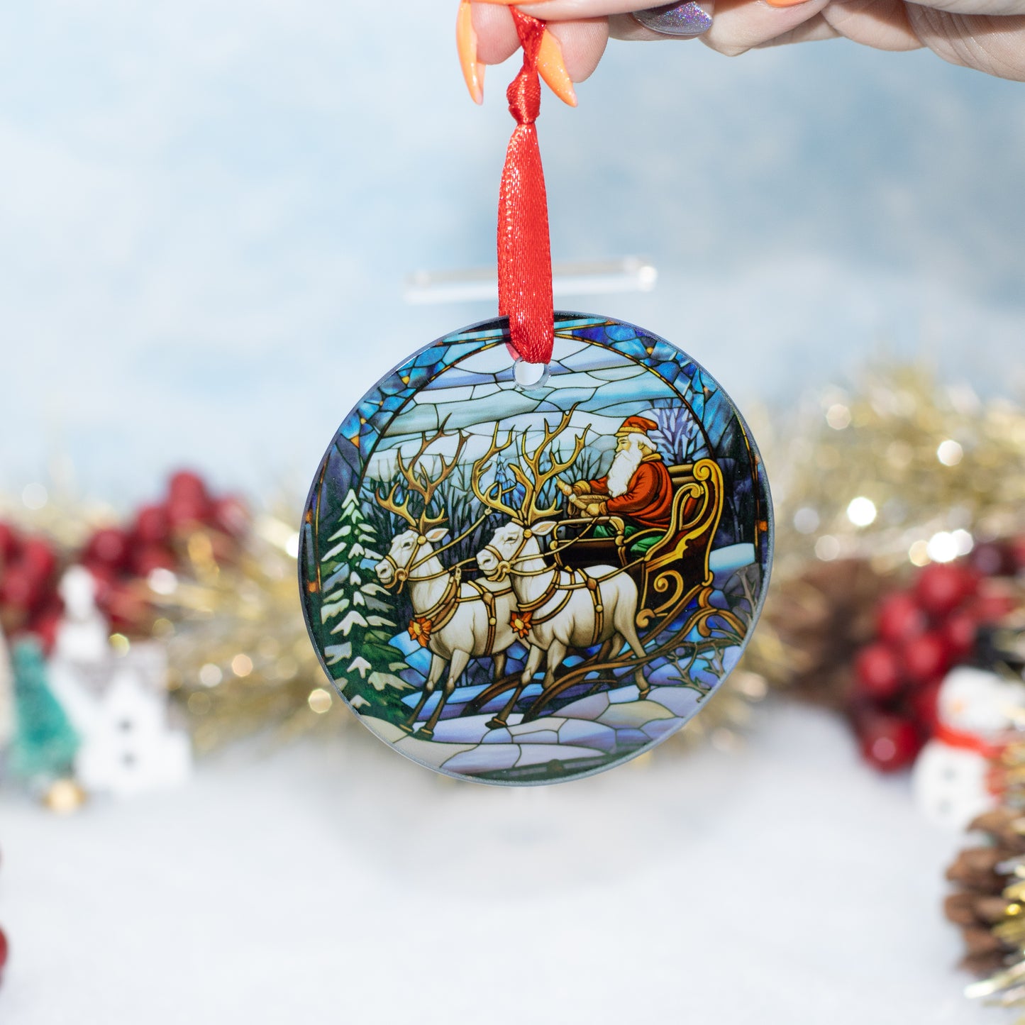 A round glass Christmas ornament featuring a stained-glass style illustration of Santa Claus riding in a sleigh with reindeer, held by a hand against a softly blurred festive background.