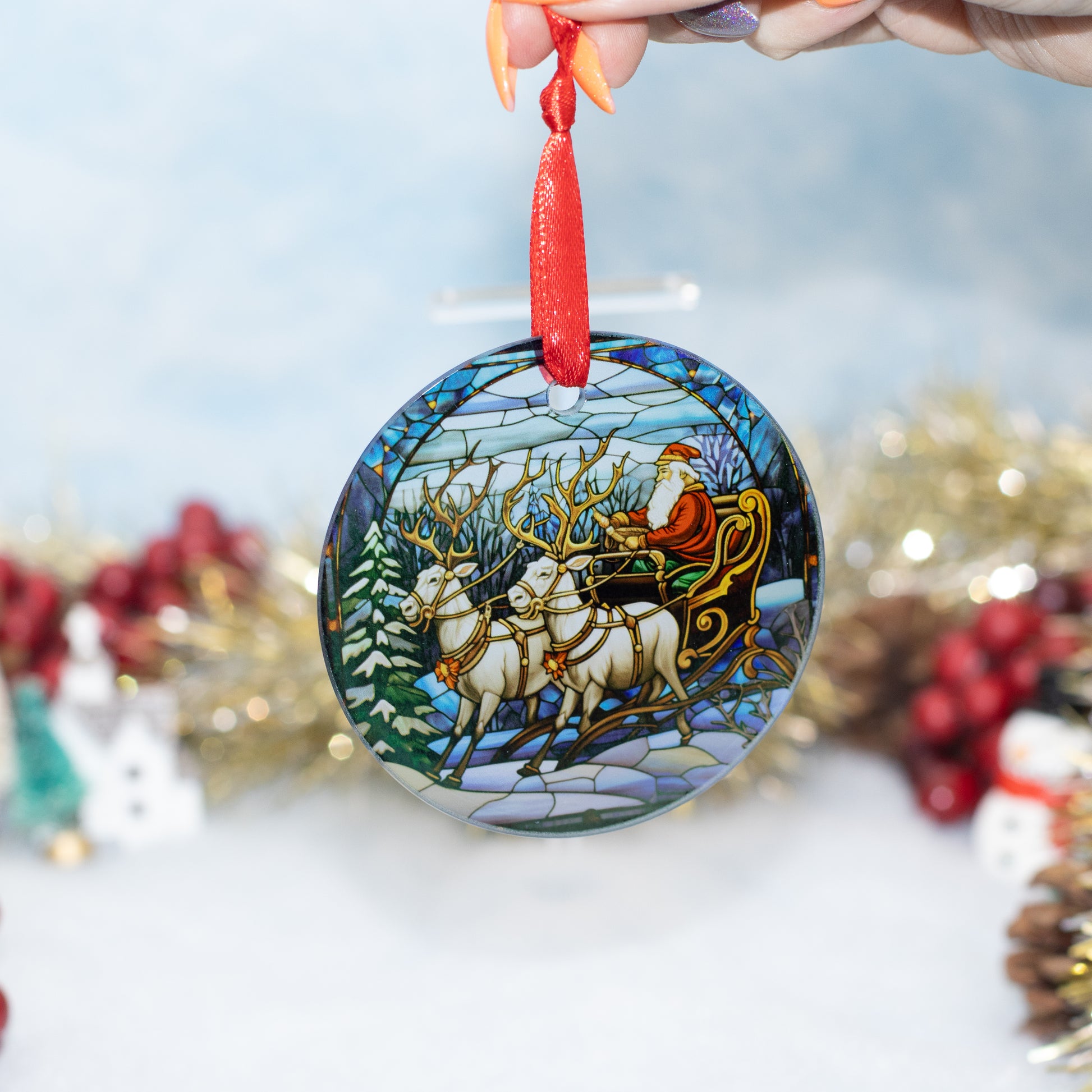A round glass Christmas ornament featuring a stained-glass style illustration of Santa Claus riding in a sleigh with reindeer, held by a hand against a softly blurred festive background.