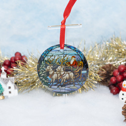 A round Christmas ornament featuring a stained-glass style illustration of Santa Claus in his sleigh with reindeer, hanging from a red ribbon against a snowy, festive background with gold tinsel and red berries.