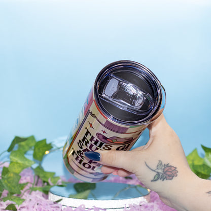 A hand holds a colourful tumbler with a clear lid, set against a light blue background with decorative green leaves and pink petals.