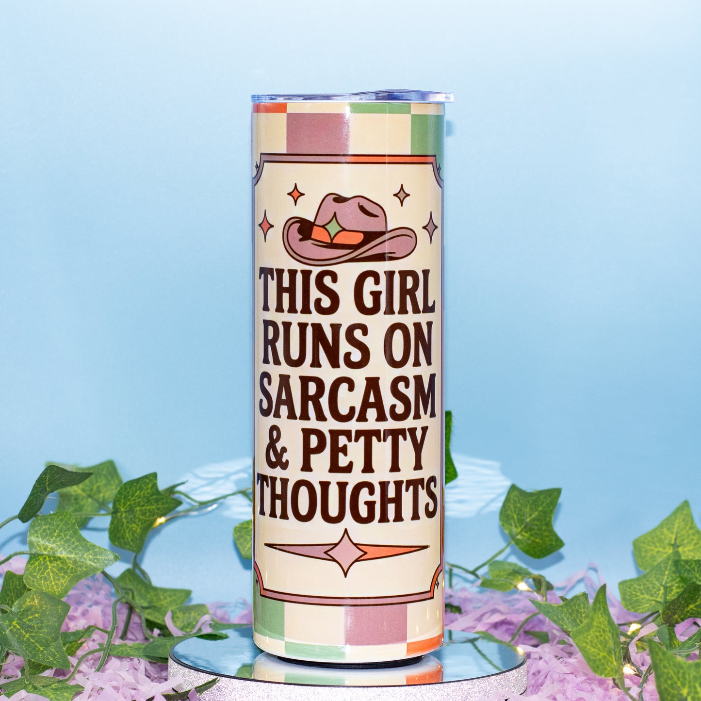 A tall cylindrical tumbler with a western-themed design, featuring the text 'THIS GIRL RUNS ON SARCASM & PETTY THOUGHTS' in dark brown lettering. The design includes a pink cowboy hat with a green star and a beige and pink checkered border.
