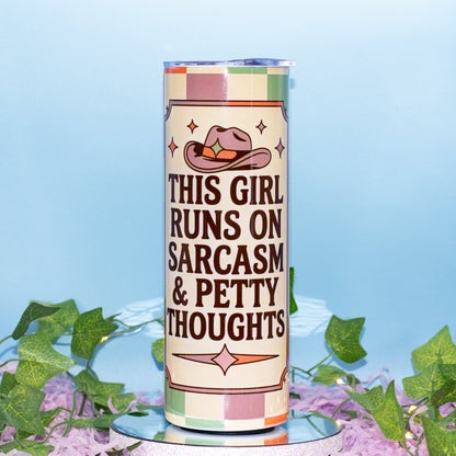 A tall cylindrical tumbler with a western-themed design, featuring the text 'THIS GIRL RUNS ON SARCASM & PETTY THOUGHTS' in dark brown lettering. The design includes a pink cowboy hat with a green star and a beige and pink checkered border.