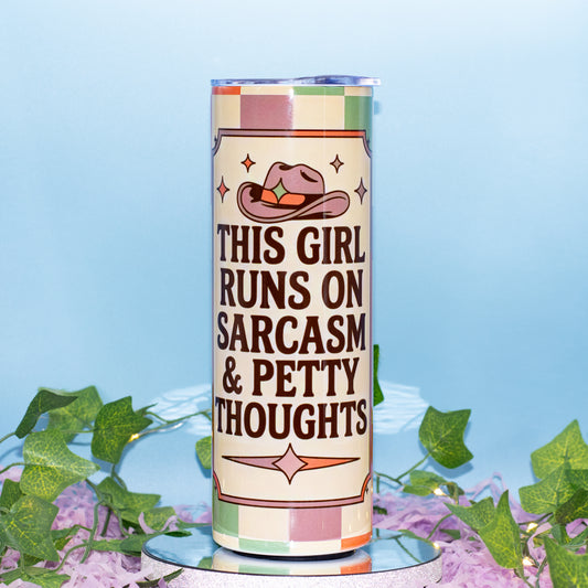 A tall cylindrical tumbler with a western-themed design, featuring the text 'THIS GIRL RUNS ON SARCASM & PETTY THOUGHTS' in dark brown lettering. The design includes a pink cowboy hat with a green star and a beige and pink checkered border.