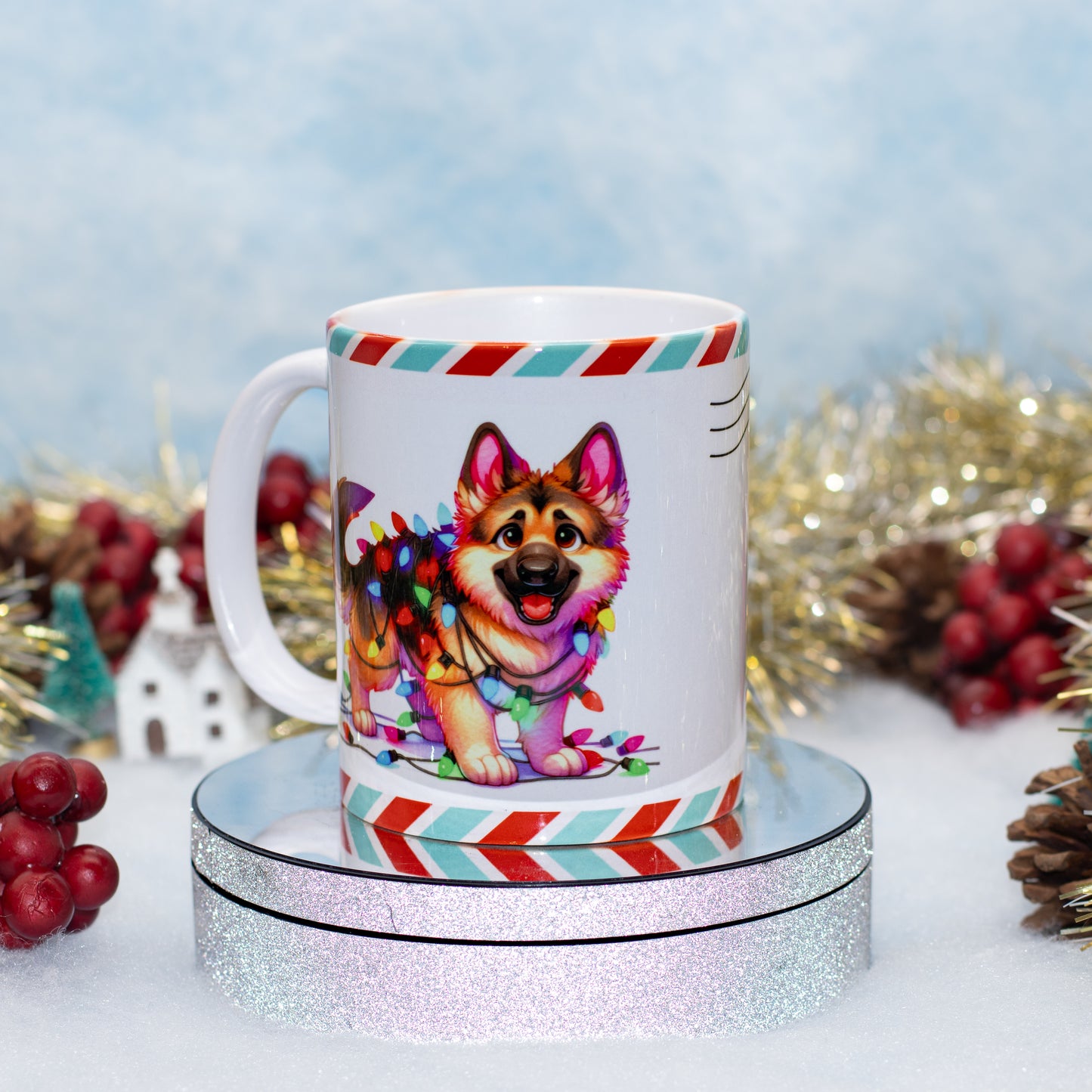 A white ceramic mug with a colorful Christmas dog illustration, displayed on a round glittery pedestal against a festive holiday background with tinsel, pinecones, and red berries.