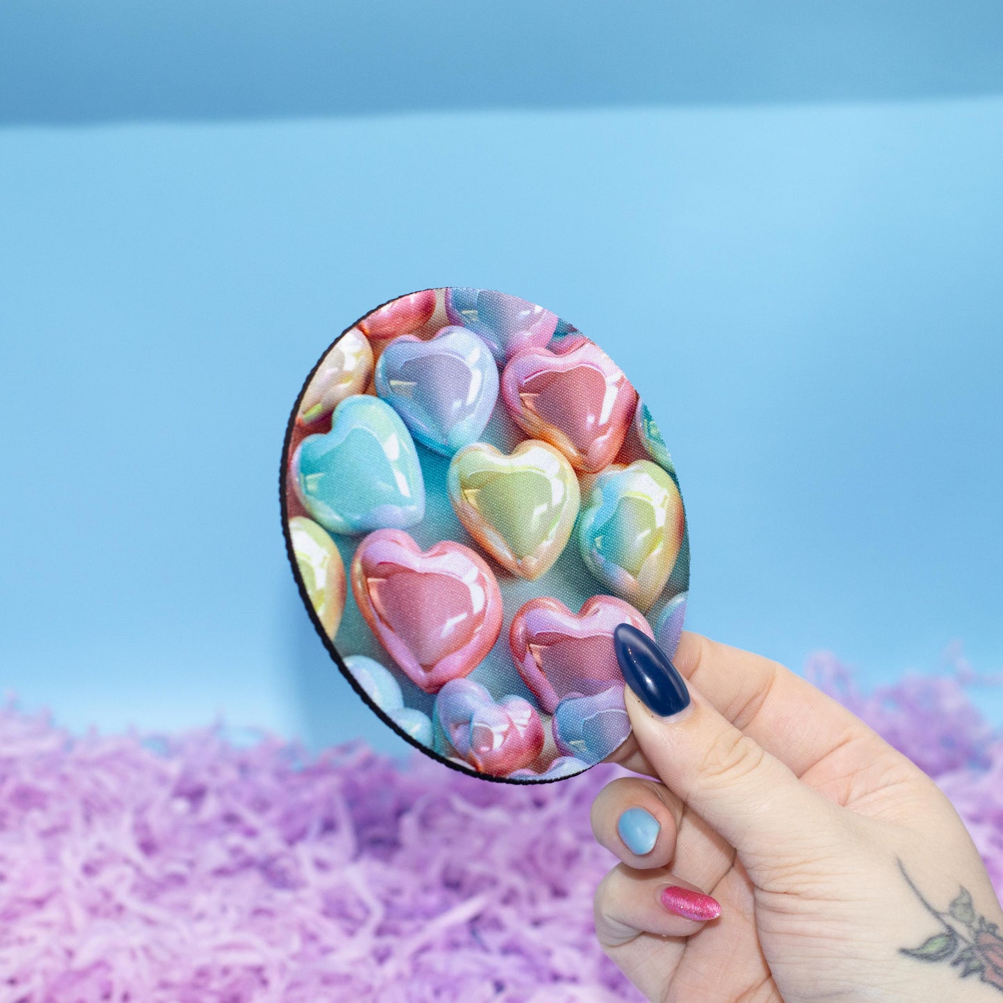 Round coaster featuring a colourful pattern of glossy heart-shaped candy set against a light blue background 