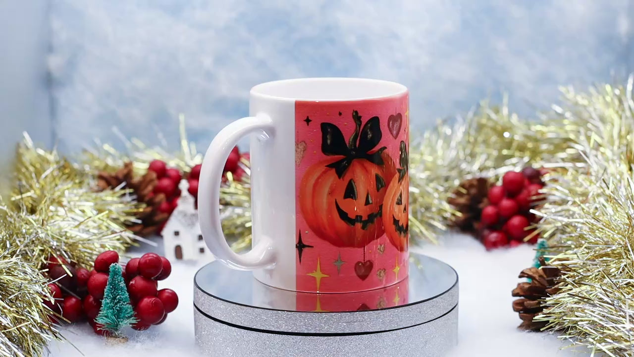 Video showing A white ceramic mug with a pink Halloween-themed print featuring jack-o'-lantern pumpkins, hearts, and stars