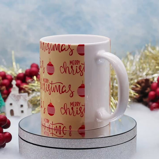 Video showing A ceramic mug wrapped in festive Christmas paper with 'Merry Christmas' and red ornaments,