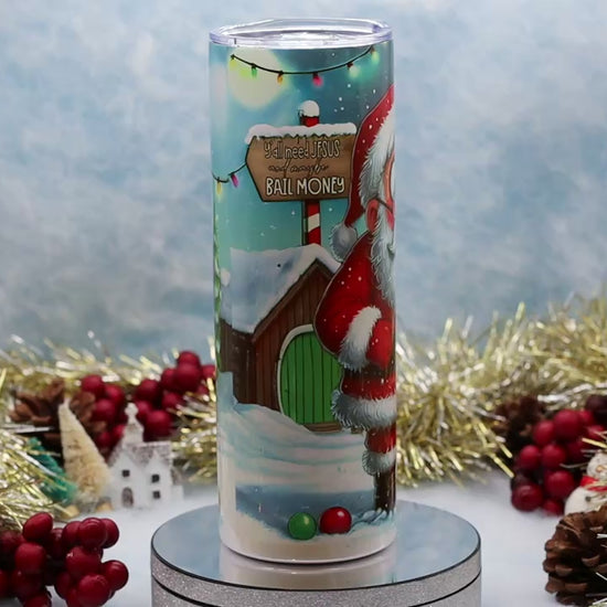 Video showcasing A Christmas Tumbler featuring Santa Claus and a scroll with names under the heading 'NAUGHTY LIST'. The candle is displayed on a silver pedestal with festive holiday decorations in the background.
