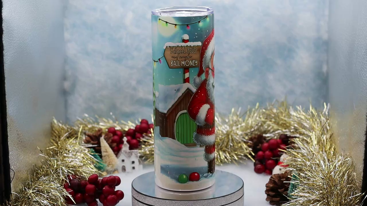 Video showcasing A Christmas Tumbler featuring Santa Claus and a scroll with names under the heading 'NAUGHTY LIST'. The candle is displayed on a silver pedestal with festive holiday decorations in the background.