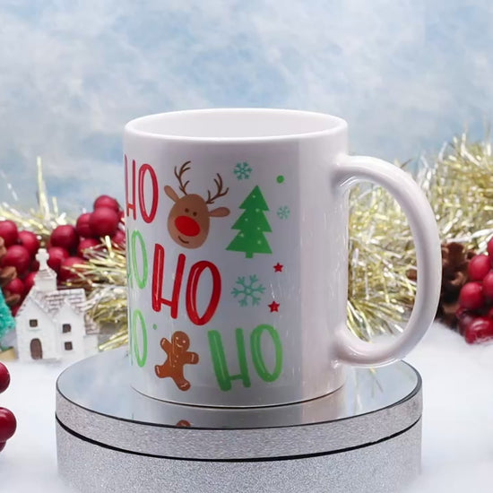 Video Showing A white ceramic mug with a festive Christmas 'Ho Ho Ho' print featuring a reindeer, candy canes, gingerbread man, and Christmas tree