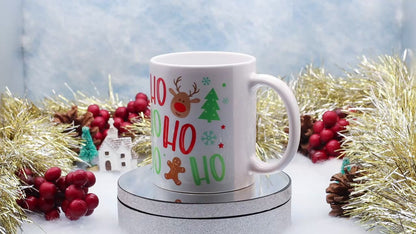 Video Showing A white ceramic mug with a festive Christmas 'Ho Ho Ho' print featuring a reindeer, candy canes, gingerbread man, and Christmas tree