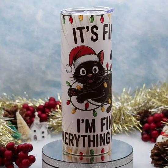 Video Showcasing A tall insulated tumbler with a clear lid, featuring a cartoon black cat in a red Santa hat and the text 'IT'S FINE I'M FINE EVERYTHING IS FINE' with holiday lights, 