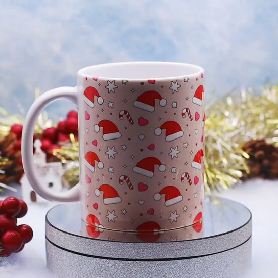 Video showcasing A white ceramic mug decorated with a festive Christmas pattern of Santa hats, candy canes, hearts, and stars,