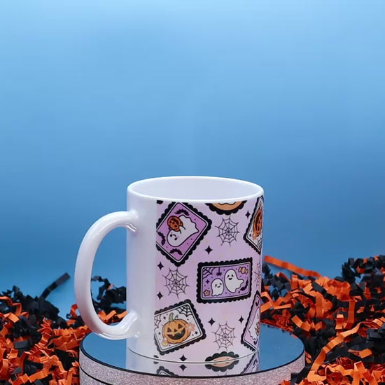 Video showcasing A white ceramic mug with a Halloween-themed pattern of candy corn, ghosts, and jack-o'-lanterns on a light pink background,
