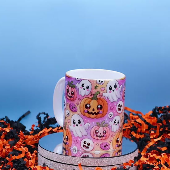 Video showingA Ceramic mug with a colourful Halloween pattern featuring cartoon pumpkins, ghosts, and skulls on a pink background