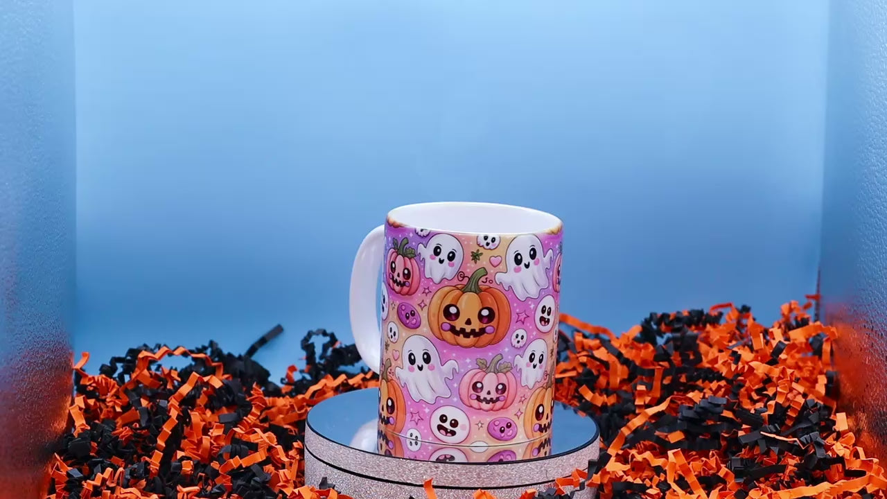Video showingA Ceramic mug with a colourful Halloween pattern featuring cartoon pumpkins, ghosts, and skulls on a pink background